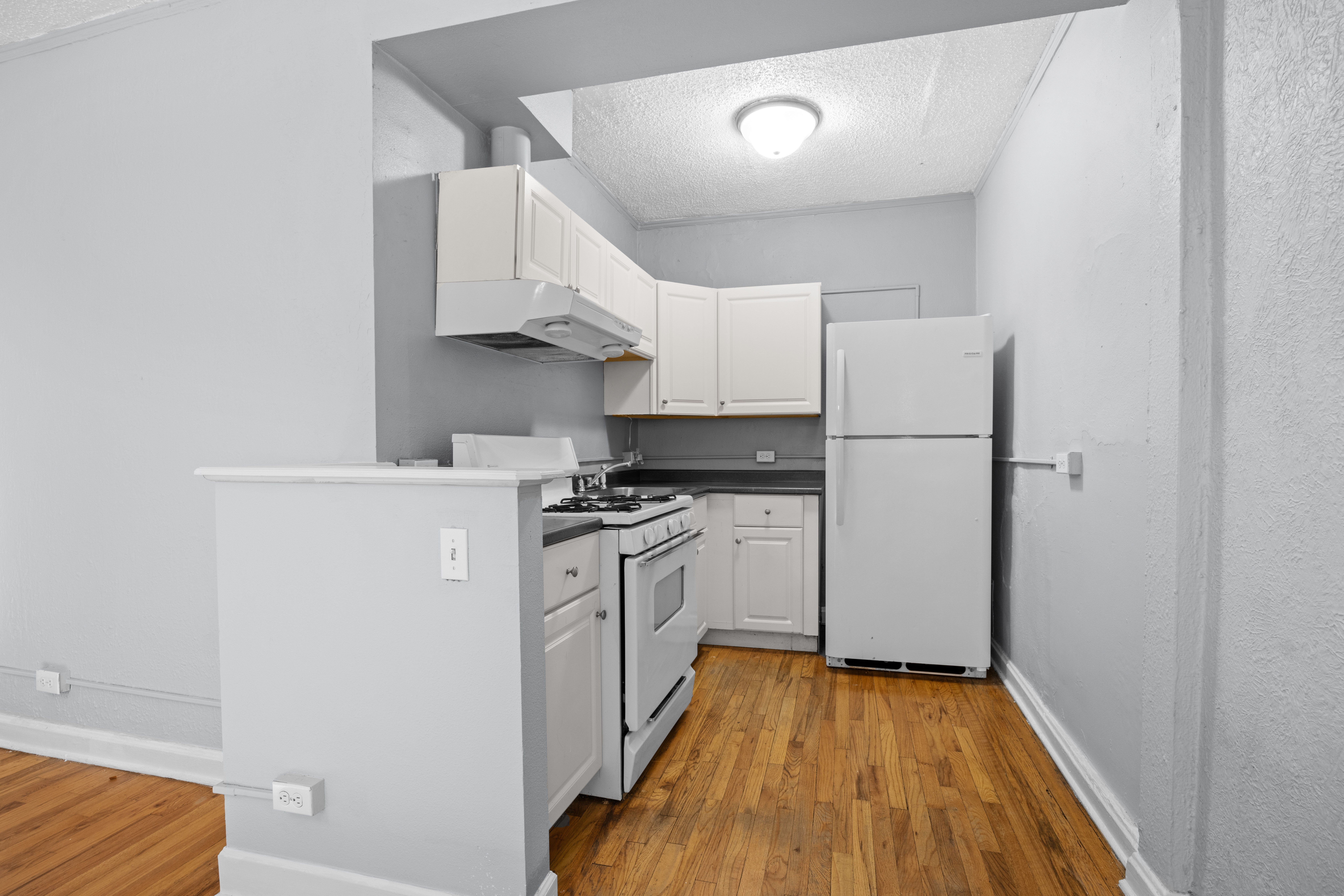 A kitchen with white appliances and wooden floors.